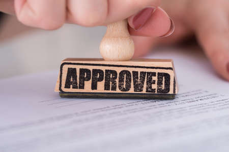 Close-up Of Person Hand Stamping Approved On Paper