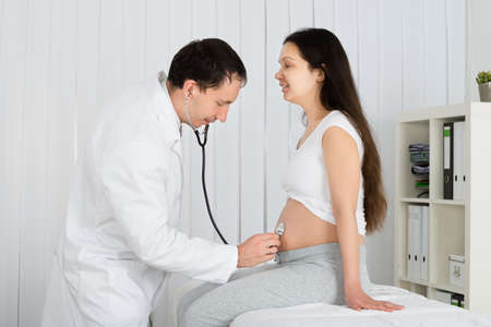 Doctor Using Stethoscope White Examining Pregnant Woman In Clinic