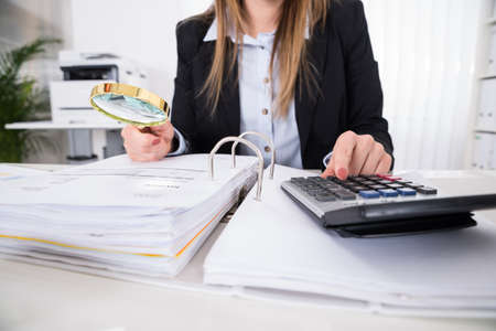 Young Businesswoman Checking Invoice With Magnifying Glass At Deskの写真素材