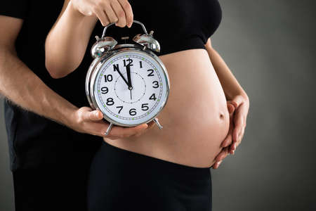 Close-up Of Pregnant Woman With Husband Showing Clockの写真素材