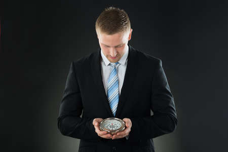 Portrait Of Young Businessman Holding Compass On Black Backgroundの写真素材