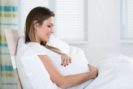 Photo Of Happy Pregnant Woman Sitting In Bedの写真素材