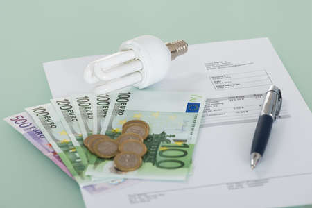 Close-up Of A Fluorescent Light Bulb With Invoice And Currencyの写真素材