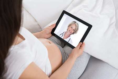 Pregnant Woman Video Conferencing With Doctor On Digital Tablet