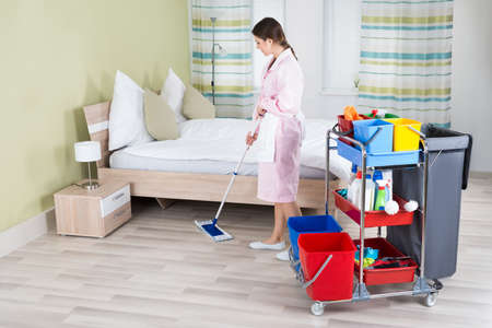 Young Female Housekeeper Mopping Floor In Roomの写真素材