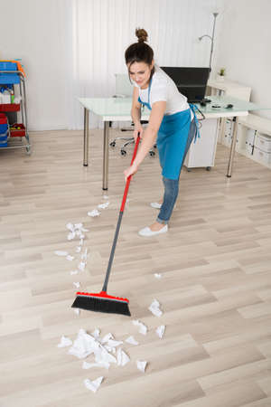 Happy Young Female Janitor Sweeping Hardwood Floor
