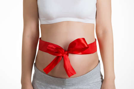 Mid Section Of Pregnant Woman's Belly Tied With Red Ribbonの写真素材