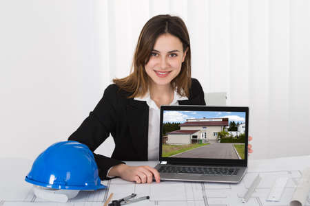 Young Female Architect Showing Picture Of House On Laptop In Officeの写真素材
