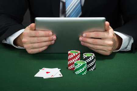 Poker Hand Holding Digital Tablet With Chips And Cards On Table