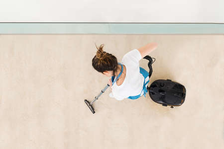 Young Female Janitor In Uniform Vacuuming Floorの写真素材