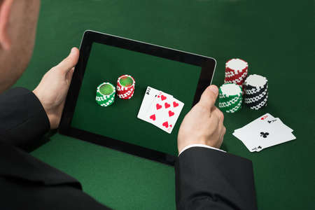 Close-up Of A Poker Hand With Digital Tablet Showing Chips And Cards