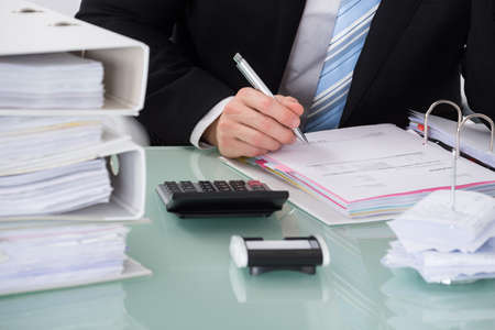 Close-up Of Businessman Calculating Invoice In Office