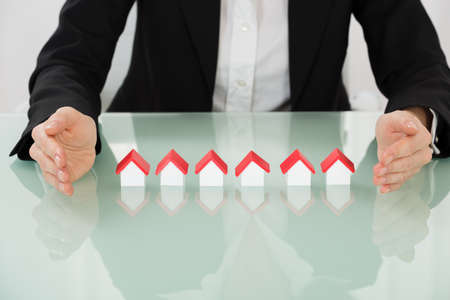 Close-up Of Businesswoman Hand Protecting House Models