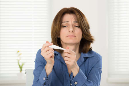 Portrait Of Sick Young Woman Looking At Thermometer