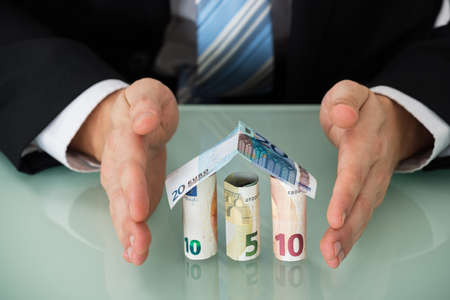 Close-up Of A Businessman Protecting House Made Of Banknotesの写真素材