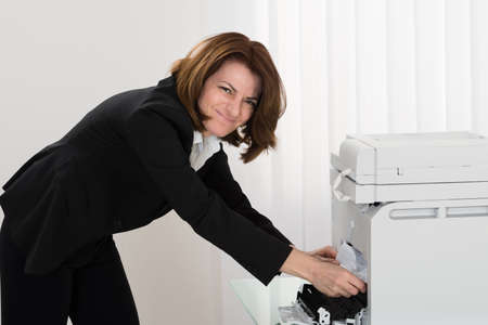 Young Businesswoman Removing Paper Stuck In Photocopy Machine At Office