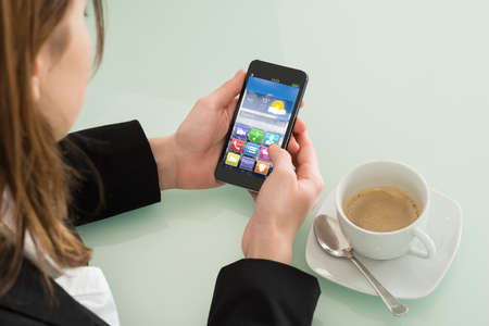 Close Up Of Businesswoman Checking Weather Forecast On Smartphone In Office