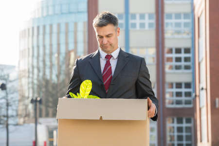 Disappointed Businessman Standing With Cardboard Box Outside Officeの写真素材