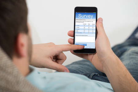 Close-up Of Young Man Filling Online Survey Form On Mobile Phoneの写真素材