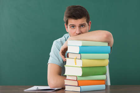 Young Man Leaning On Stack Of Books At Deskの写真素材