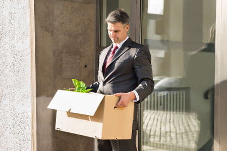 Sad Mature Businessman Moving Out With Cardboard Box From Officeの写真素材