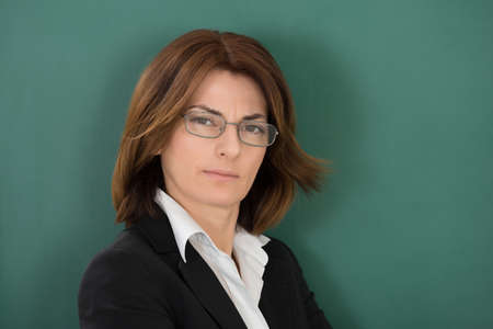 Portrait Of Young Female Teacher Standing Against Green Chalkboardの写真素材
