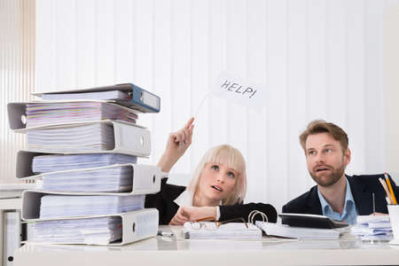 Two Young Businesspeople Holding White Flag With Help Text In Office