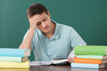 Tired Young Man With Books At Desk In Classroom