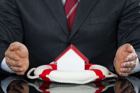 Close-up Of Businessman Hand Protecting House Model With Lifebelt At Deskの写真素材