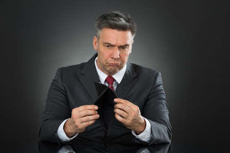 Sad Businessman With Empty Wallet Sitting At Desk Against Gray Backgroundの写真素材