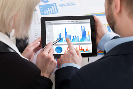 Two Businesspeople Analyzing Graph On Digital Tablet In Office