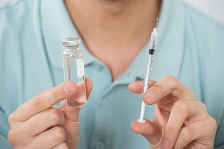 Close-up Of Young Man Holding Medicine Bottle And Syringe