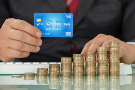 Businessman Using Credit Card And Keyboard With Stacked Coins Arranged At Office Desk