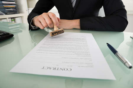 Close-up Of Businessman Hand Stamping Approved On Contract Paperの写真素材