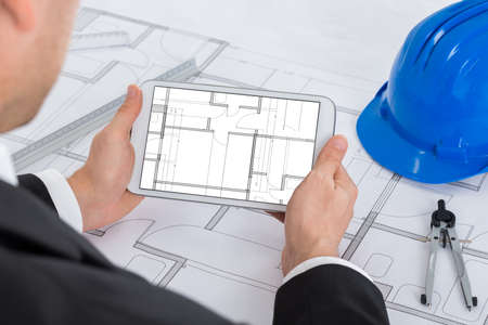 Male Architect Analyzing Blue Print On Digital Tablet In Officeの写真素材