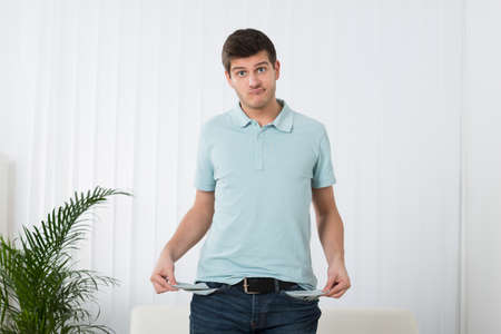 Sad Young Man Showing Empty Pockets At Homeの写真素材