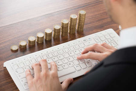Businessman Working On Keyboard With Coins Stackedの写真素材