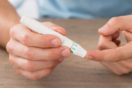Close-up Of Young Man Checking Blood Sugar Level With Glucometer At Desk