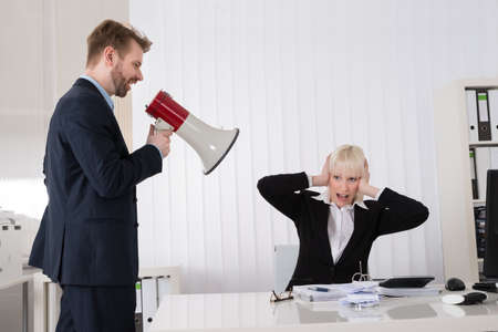 Boss Shouting At Young Businesswoman Through Loudspeaker In Officeの写真素材