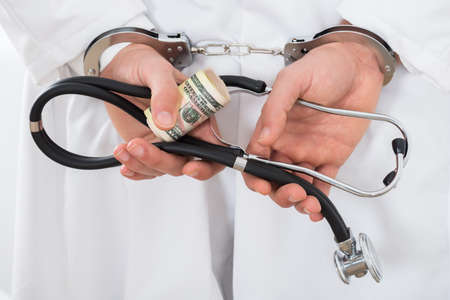 Close-up Of A Doctor Hands Holding Bank Notes And Handcuffsの写真素材