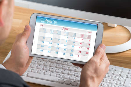 Close-up Of Young Businessman Using Calendar On Digital Tablet At Computer Deskの写真素材