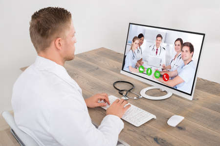 Young Male Doctor Video Conferencing With Medical Team On Computer Desk In Clinic