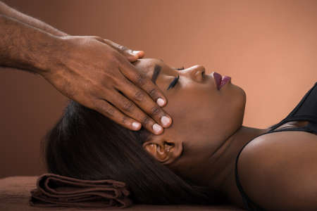 Relaxed Young African Woman Receiving Forehead Massage In Spaの写真素材