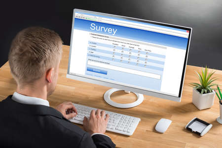 Close-up Of Young Businessman Filling Online Survey Form On Computer At Desk