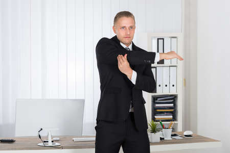 Portrait Of A Young Businessman Stretching In Office