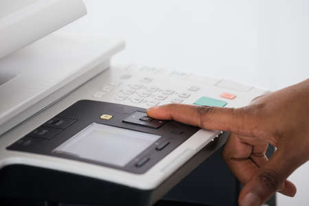 Close-up Of Young Businesswoman Hand Pressing Printer's Button In Officeの写真素材