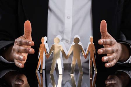 Close-up Of Businessperson Protecting Cut-out Figures On Deskの写真素材