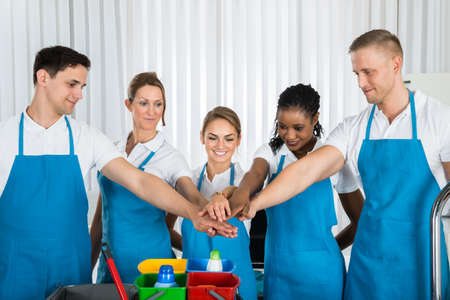 Group Of Happy Cleaners In Uniform Stacking Hands At Workplace