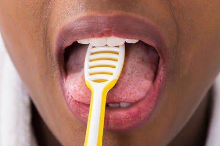 Close-up Of Young Woman Cleaning Tongue With Cleaner