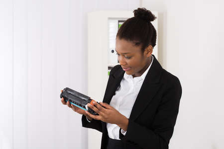 Young African Businesswoman Looking At Cartridge In Office